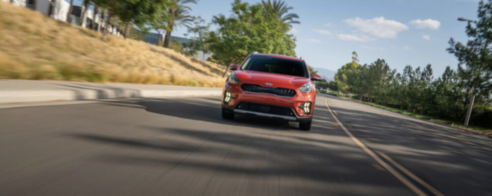 Red 2021 Kia Niro driving down tree-lined road